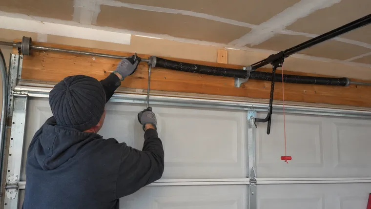 Technician winding a garage door torsion spring with steel winding bars, door closed